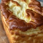 A close-up of a golden-brown loaf of Keto Cottage Cheese Cloud Bread, showing its fluffy, cloud-like top texture. The loaf is sitting on crumpled parchment paper with a blurred background.