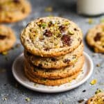 A delicious stack of four homemade pistachio chocolate chip cookies on a white plate, topped with chopped pistachios and flaky sea salt.