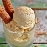 Creamy homemade Horchata Ice Cream served in a clear glass, garnished with a sprinkle of cinnamon and two rolled wafer cookies, on a rustic wooden surface